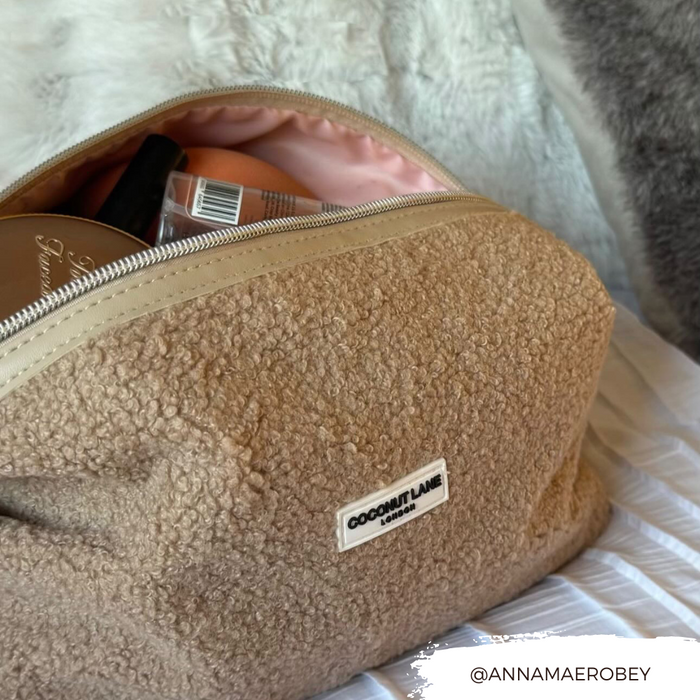 Partially unzipped Coconut Lane Teddy Rupert expandable makeup bag on a white bedspread.