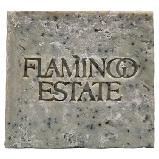 A single rectangular bar of handmade soap with a rustic, textured surface speckled with dark flecks. The brand name 'FLAMINGO ESTATE' is embossed in the center of the soap.