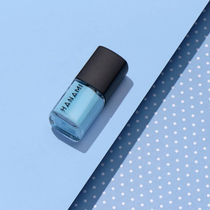 Blue nail polish bottle with black cap on a light blue background.