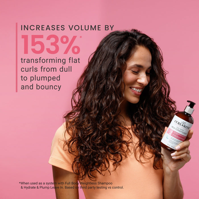 Woman with curly hair holding a bottle of shampoo against a pink background