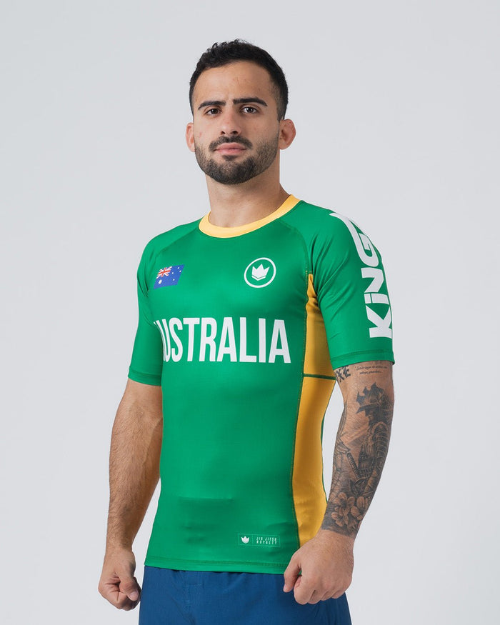 Kingz Jersey Rashguard Australia Edition - Full Body 3/4 Front View Male Athlete Short Sleeve Green Body AUSTRALIA Text Australian Flag Crown Logo Yellow Gold Side Stripe Right KINGZ Sleeve Text JIU JITSU ROYALTY Lower Hem BJJ [color:Green/Austria]