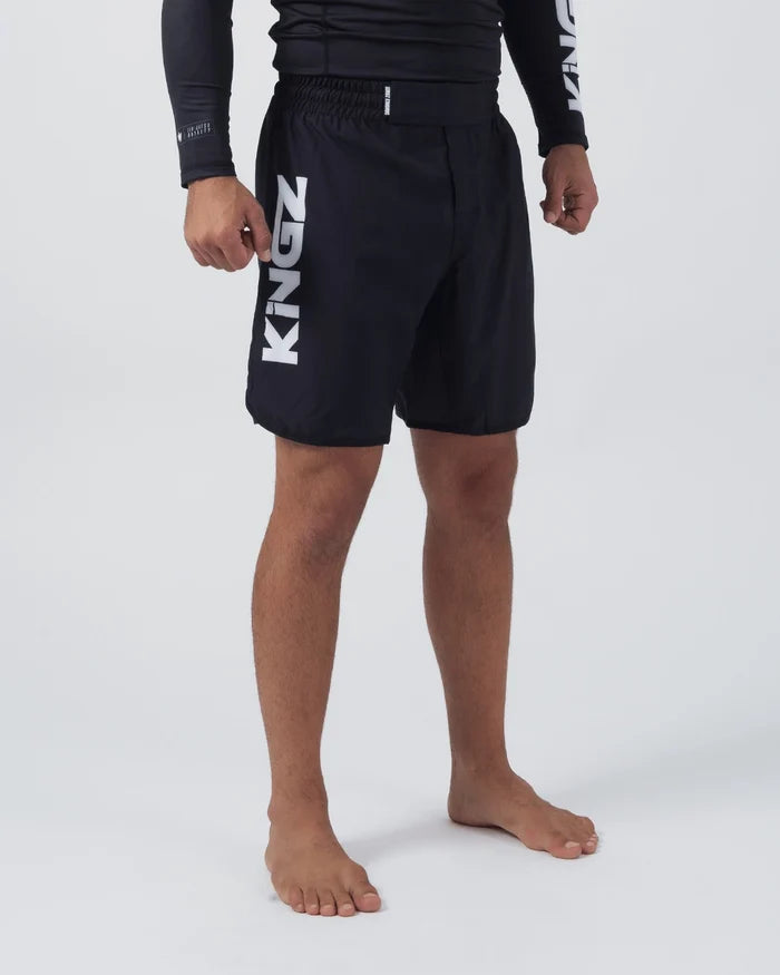 Kingz Kore V2 Shorts Black - 3/4 Angled Front View Male Athlete Black Grappling Shorts Large KINGZ White Text Left Outer Thigh Elastic Waistband Competition Cut Black KINGZ Rashguard White Text Sleeve Bare Feet Men's No-Gi BJJ MMA Kore Collection [color:Black]