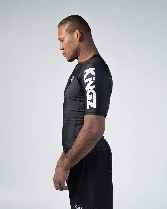 Kingz Kore V2 Short Sleeve Rashguard Black - Side Profile View Male Athlete White KINGZ Sleeve Text Black Crown Badge Fitted Design BJJ No-Gi Grappling Rash Guard [color:Black]