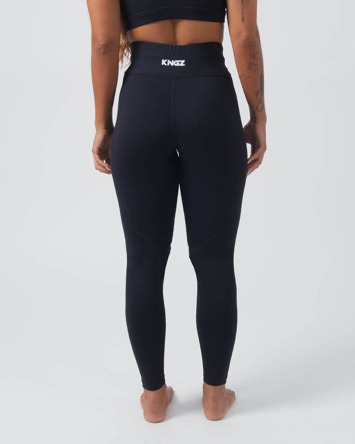 Kingz Kore Women's Grappling Spats Black - Full Body Left Side Profile Alternate Stance Female Athlete All-Black KINGZ White Waistband Text KINGZ White Vertical Calf Text High-Waist Women's No-Gi BJJ Spats Kore Collection [color:Black]