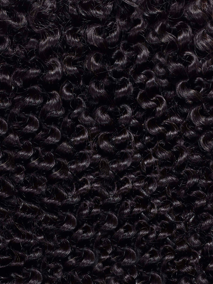 Close-up of tightly coiled, dark brown to black curly hair filling the frame, creating a textured, wavy pattern with natural depth.