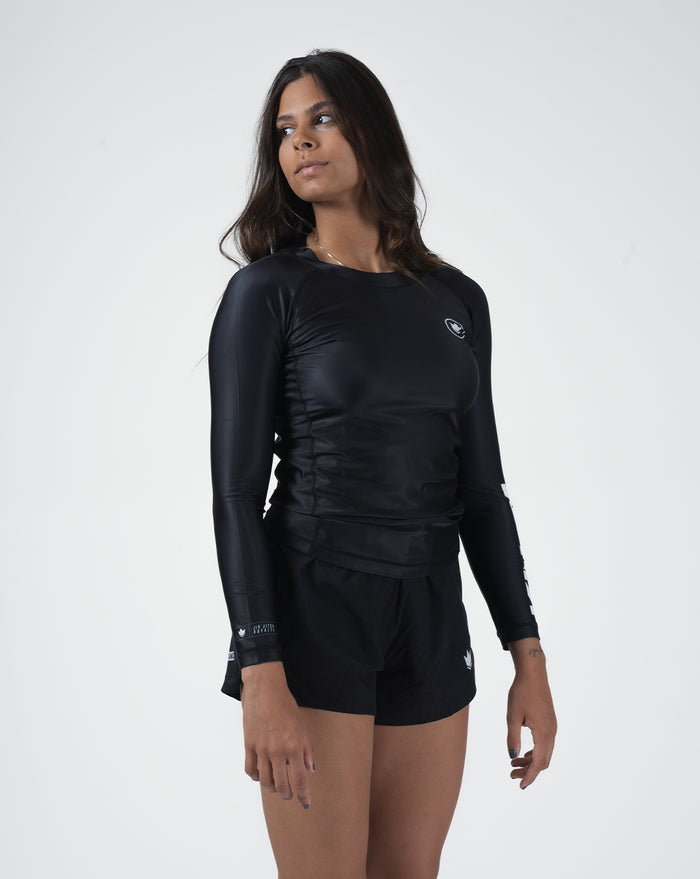 Kingz Kore V2 Long Sleeve Rashguard Black - Full Body 3/4 Front Left Side View Female Athlete Long Sleeve All Black Body Crown Logo Circle Chest KINGZ KIMONOS EST 2011 White Left Sleeve Text Matching Black Shorts BJJ Women's No-Gi Kore [color:Black]