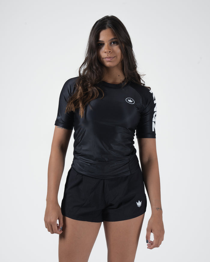 Kingz Kore V2 Short Sleeve Rashguard Black - Full Body Front View Female Athlete Short Sleeve All Black Minimal Design White Crown Logo Circle Chest KINGZ White Sleeve Text Matching Black Shorts Crown Logo Women's BJJ No-Gi Kore V2 [color:Black]