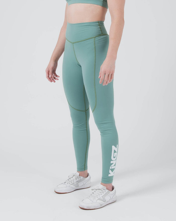 Kingz Kore Women's Grappling Spats Green - Full Body Right Side Profile Female Athlete Sage Teal Green KINGZ White Vertical Text Right Calf Side Seam Detail High-Waist Compression Fit Women's No-Gi BJJ Spats Kore Collection [color:Sage Green]