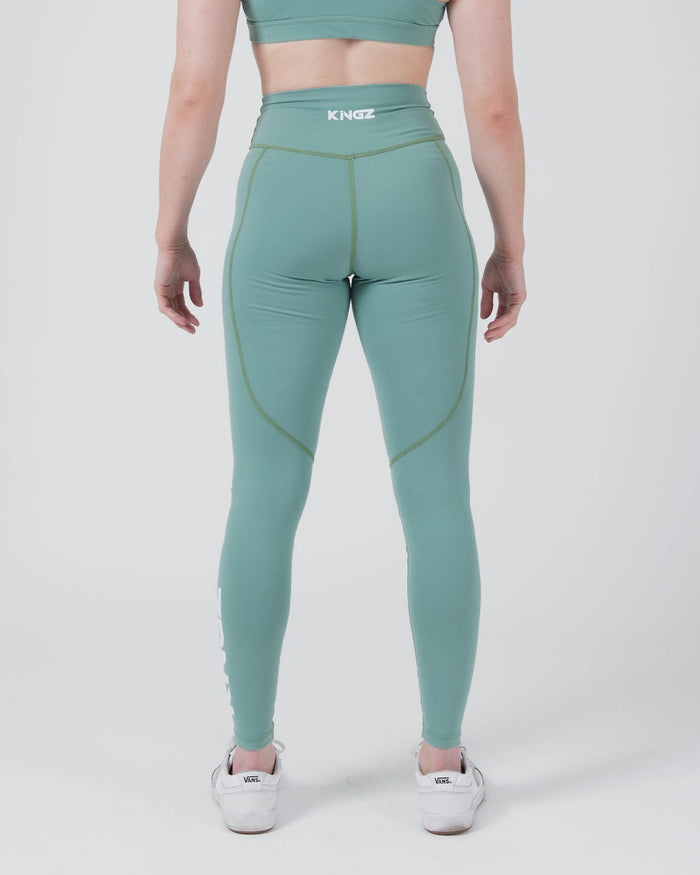 Kingz Kore Women's Grappling Spats Green - Full Body Back View Female Athlete Sage Teal Green KINGZ White Text Back Waistband Rear Seam Detail KINGZ Right Calf Text Visible Women's No-Gi BJJ Spats Kore Collection [color:Sage Green]