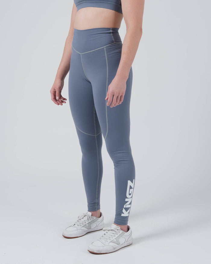 Kingz Kore Women's Grappling Spats Smoke Blue - Full Body Right Side Profile Female Athlete Slate Smoke Blue KINGZ White Vertical Text Right Calf V-Seam Front Detail High-Waist Full-Length Compression Fit Women's No-Gi BJJ Spats Kore Collection [color:Steel Blue]