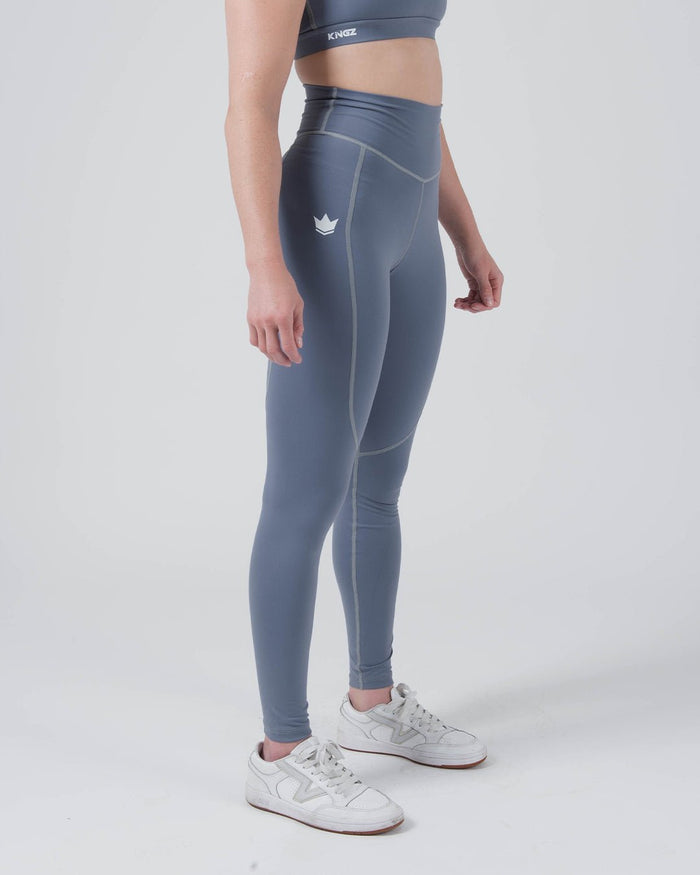 Kingz Kore Women's Grappling Spats Smoke Blue - Full Body Left Side Profile Female Athlete Slate Smoke Blue Small White Crown Logo Left Thigh Side Pocket Seam High-Waist Full-Length Compression Fit Women's No-Gi BJJ Spats Kore Collection [color:Steel Blue]