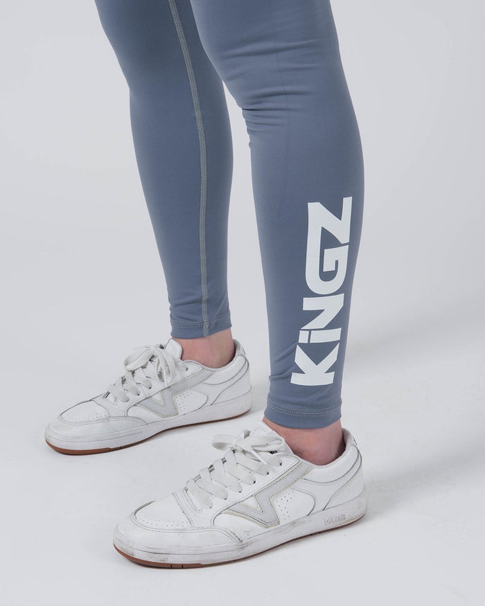 Kingz Kore Women's Grappling Spats Smoke Blue - Close Up Leg Detail KINGZ Large White Vertical Text Right Calf Slate Smoke Blue Seam Detail White Vans Sneakers Gum Sole Women's No-Gi BJJ Spats Kore Collection Branding Detail [color:Steel Blue]