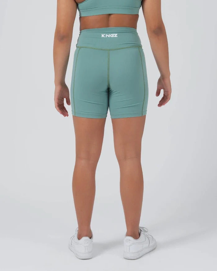 Kingz Kore Women's Training Shorts Green Light Sage - Full Body Back View Female Athlete Sage Mint Green Biker Style Short Cut High-Waist KINGZ White Text Center Back Waistband Olive Green Contrast Side Seam Stitching Smooth Back Panel Matching Sage Sports Bra White Sneakers Women's Training Shorts No-Gi BJJ Kore Collection [color:Light Green]
