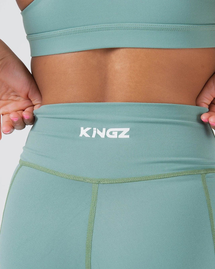 Kingz Kore Women's Training Shorts Green Light Sage - Close Up Waistband Detail KINGZ White Text Front Center Wide High-Waist Waistband Hands on Hips Pose Sage Mint Green Fabric Olive Green Contrast Stitching Women's Training Shorts No-Gi BJJ Kore Collection [color:Light Green]