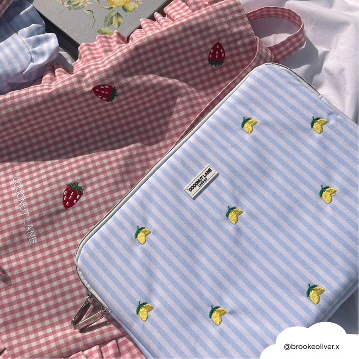 Pink gingham iPad sleeve with strawberry embroidery next to a yellow lemon-print Coconut Lane laptop sleeve.
