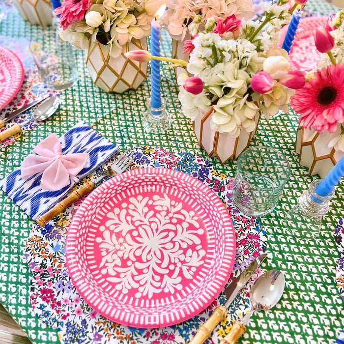 Colorful table setting with pink plates, floral arrangements, and decorative elements on a green patterned tablecloth.