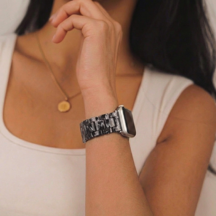 Woman wearing a gold pendant necklace and a black marble-patterned Apple Watch strap with gold hardware.