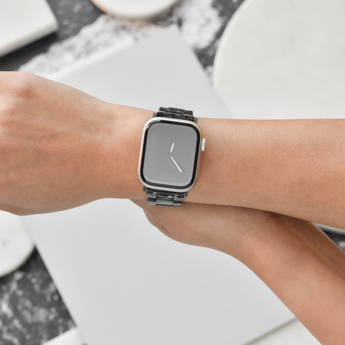 A close-up image of a person's wrist adorned with a sleek, modern smartwatch featuring a minimalist black rectangular face paired with the Luxe Black Marble Apple Watch Strap from Coconut Lane. The watch is elegantly displayed against a neutral background with Luxe Black Marble textures.