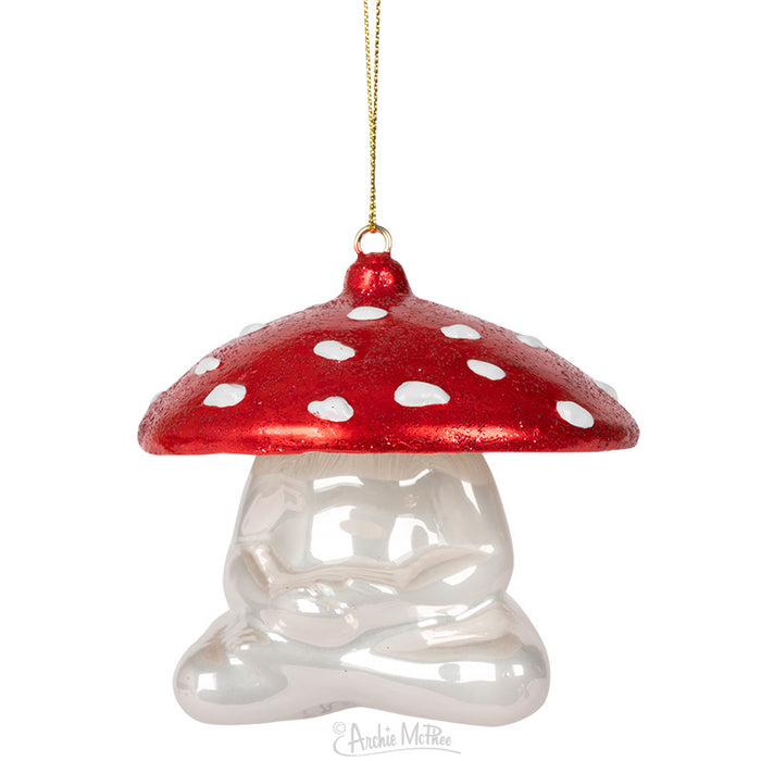 The Meditating Mushroom Ornament, crafted from hand-blown glass, showcases a red and white design with a shiny, reflective base. Suspended elegantly by a golden string, it brings charm to any space.