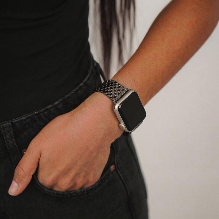 Person wearing black top and jeans shows a black mermaid-pattern Apple Watch strap with hand in pocket.