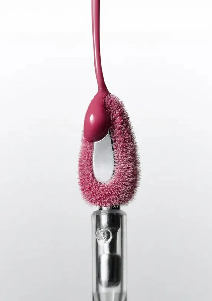 Pink cleaning brush with bristle head attached to a clear cylindrical handle on a white background