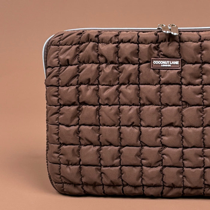 Quilted chocolate brown laptop sleeve with zipper and Coconut Lane label on a brown background.