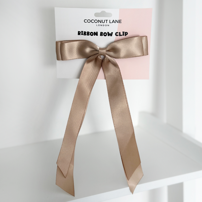 Caramel nude ribbon bow hair clip by Coconut Lane on its display card, resting on a white shelf.