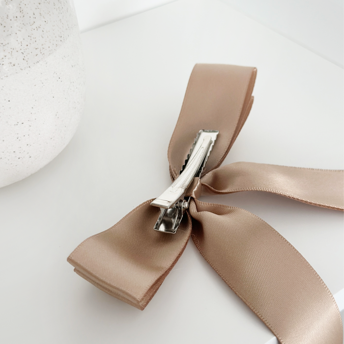 Caramel nude ribbon bow hair clip by Coconut Lane on a white surface next to a speckled white vase.
