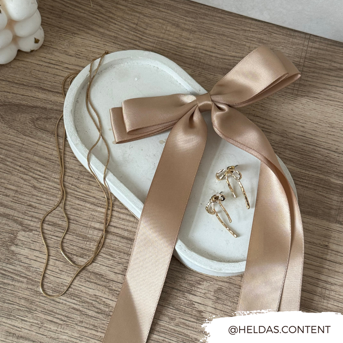 Gold necklace and earrings with a satin bow next to Coconut Lane caramel nude ribbon bow clip on wood background.