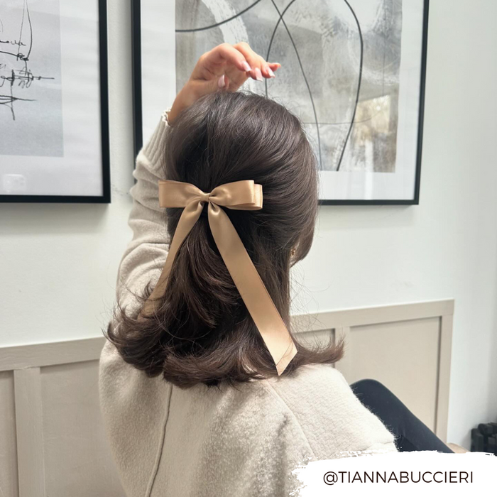 Woman with shoulder-length brown hair wears a caramel nude ribbon bow hair clip in a modern room.