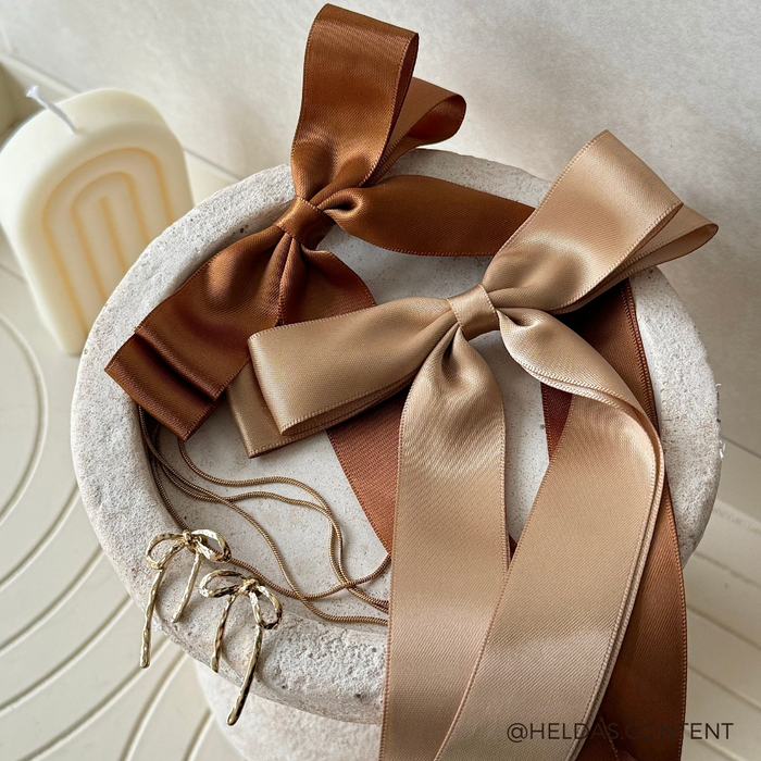 Brown and beige satin bows, gold hoop earrings, and a caramel nude ribbon bow hair clip displayed together.
