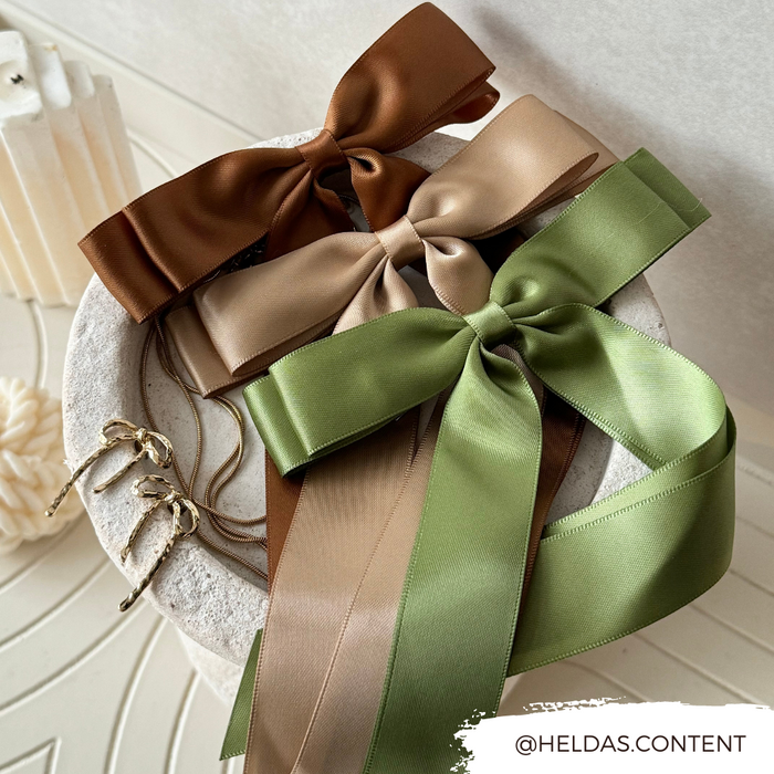 Khaki, beige, and green ribbon bow hair clips displayed next to a pair of gold earrings.