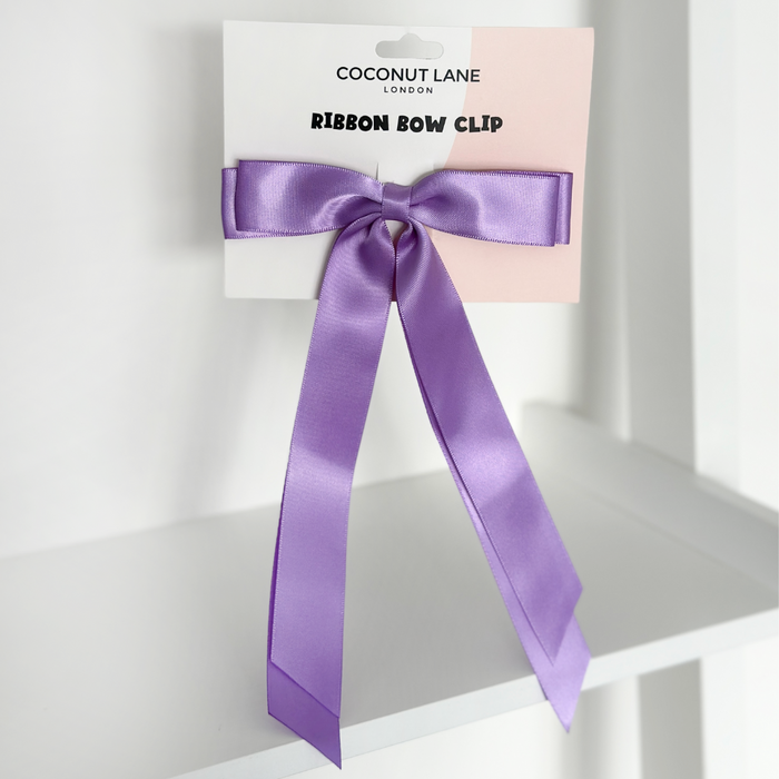 Hyacinth purple ribbon bow hair clip by Coconut Lane on a white shelf.