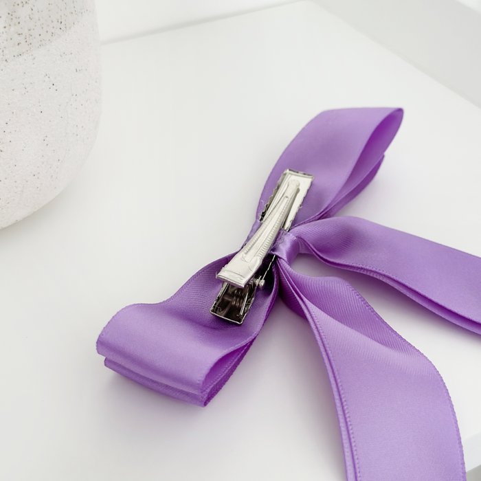 Hyacinth Purple satin ribbon bow clip with metal clasp, displayed on a white surface next to a textured object.