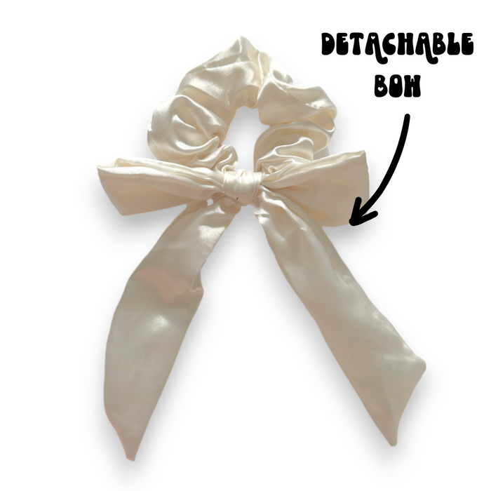 Satin bow scrunchie in almond cream with a detachable bow, featuring a smooth, glossy finish.