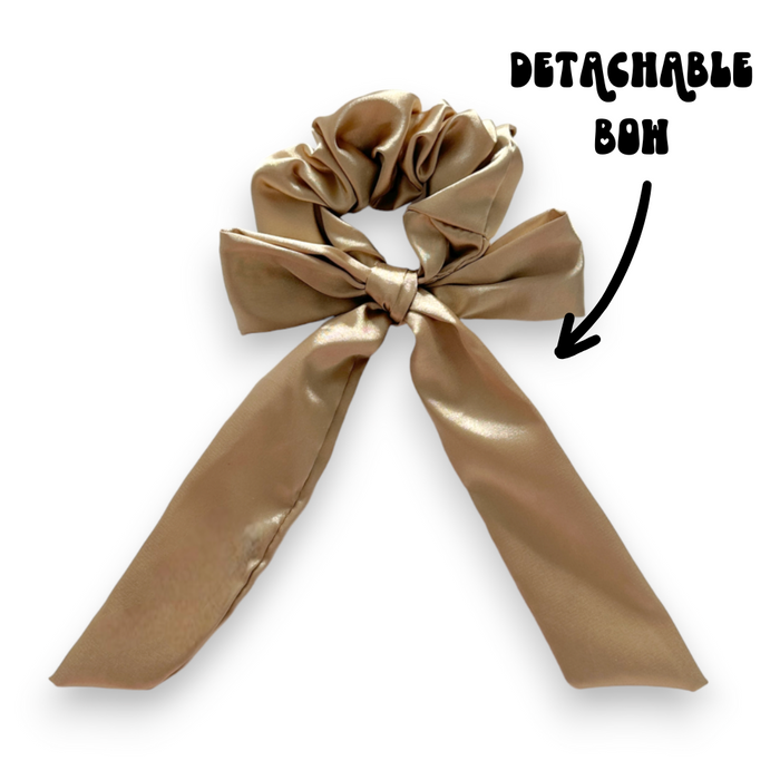 Caramel nude satin scrunchie with a detachable bow, shown alongside black arrow and text.