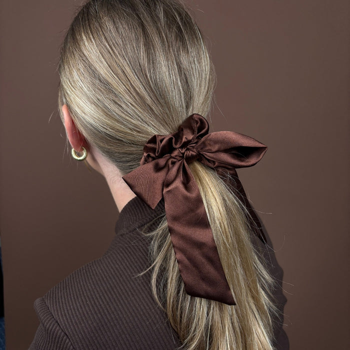 Blonde woman wears a chocolate brown satin bow scrunchie, securing her ponytail.