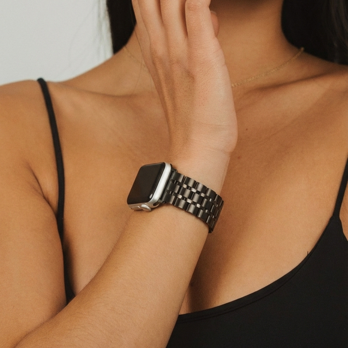 Woman in a black tank top wearing a black stainless steel Apple Watch strap, touching her chin.