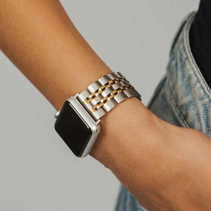 Stainless steel Apple Watch strap in silver and gold on wrist, paired with blue denim jeans.