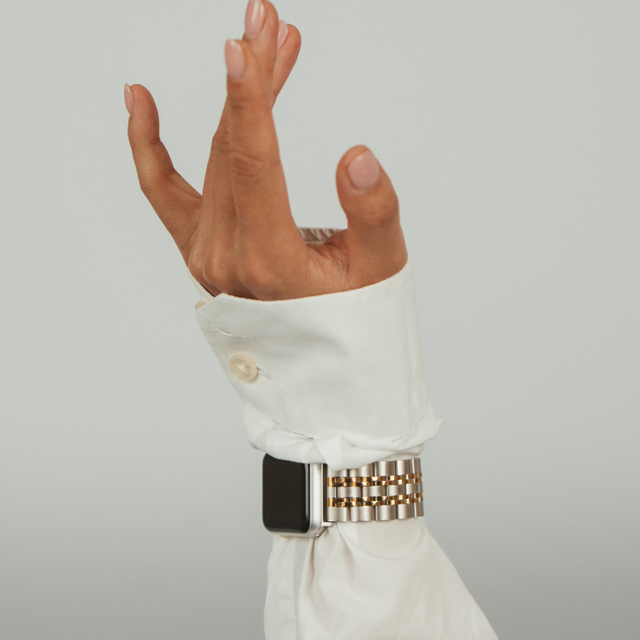 Silver and gold stainless steel Apple Watch strap on wrist, worn with a white shirt sleeve.