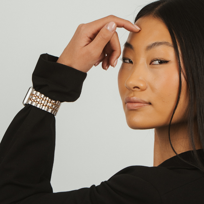 Woman in a black blazer wears a silver and gold stainless steel Apple Watch strap.