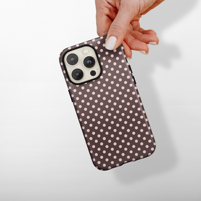 Hand holding a Coconut Lane Tough MagSafe phone case in brown with white polka dots.
