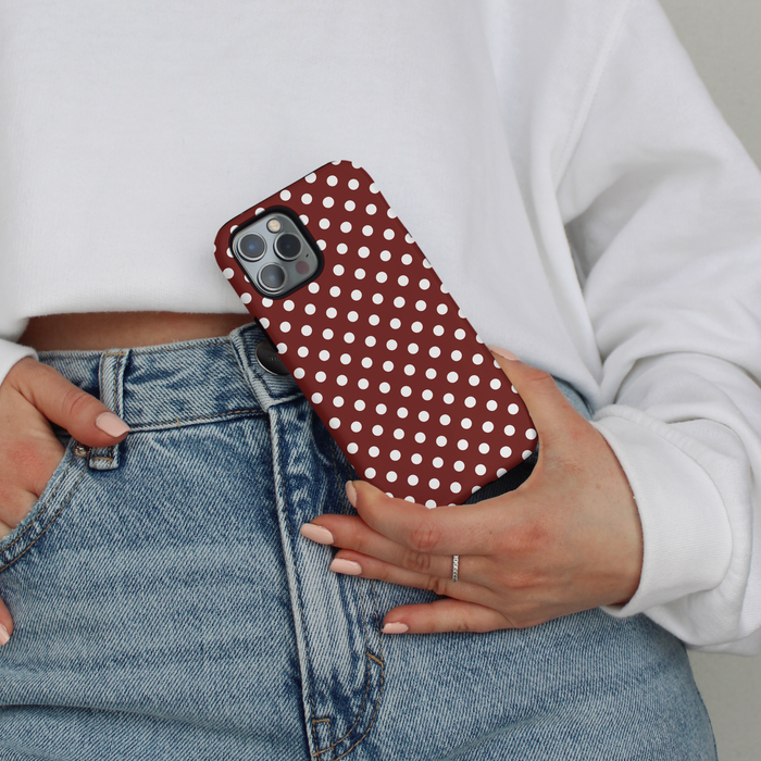 Person in blue jeans and white sweatshirt holding a burgundy polka dot phone case by their waist.