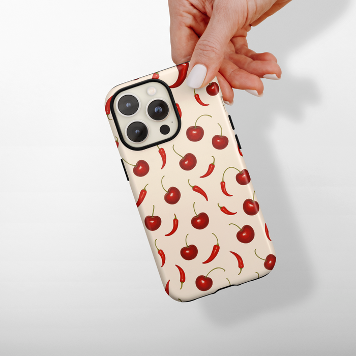 Hand holding Coconut Lane Tough MagSafe phone case with red cherry and chili pepper pattern.