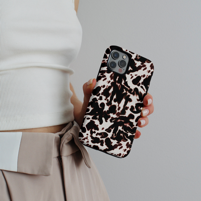 Person in white top and beige pants holding a white tortoiseshell Coconut Lane Tough Phone Case.