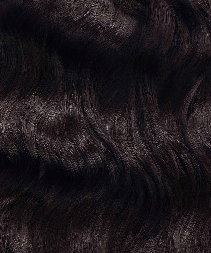 Close-up of shiny, wavy, dark brown or black hair with a smooth texture and natural waves, showcasing healthy locks.