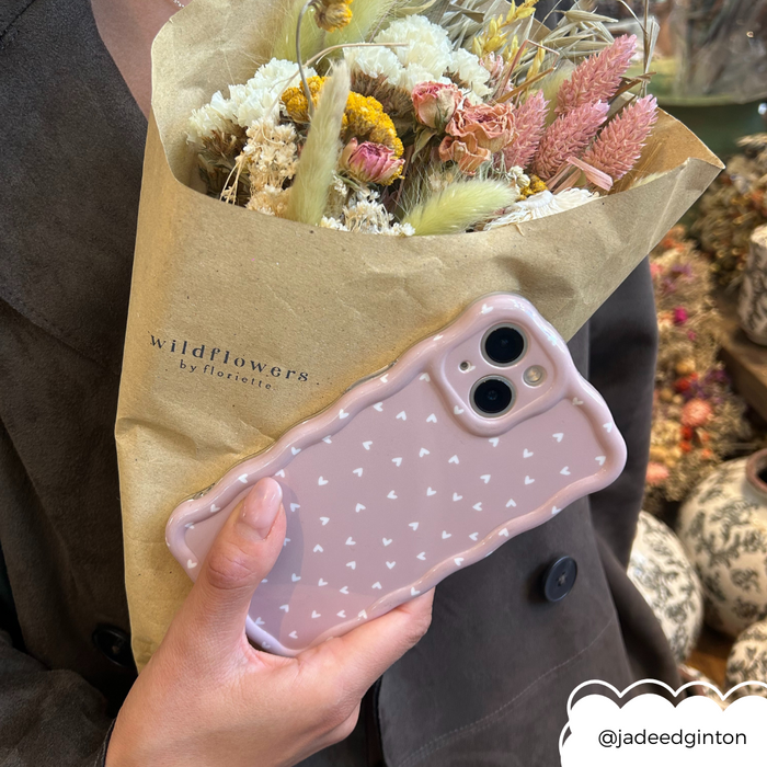 Hand holding dried wildflowers and a Coconut Lane chai hearts wavy phone case with beige and heart pattern.