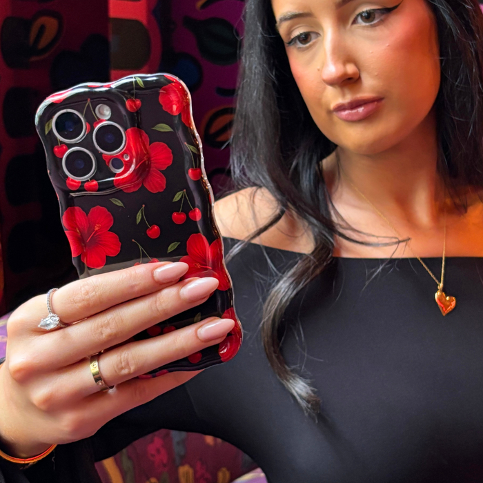 Woman with long dark hair holds a wavy phone case with red and pink cherry hibiscus pattern, wearing a black top.