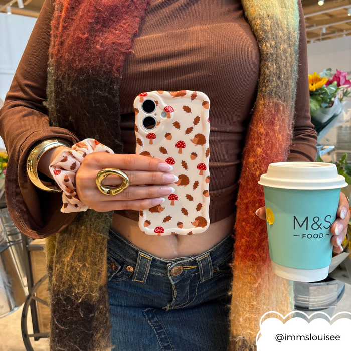 Woman in a brown top holds coffee and a phone with Coconut Lane’s green wavy Forest Friends case, plus scarf and scrunchie.