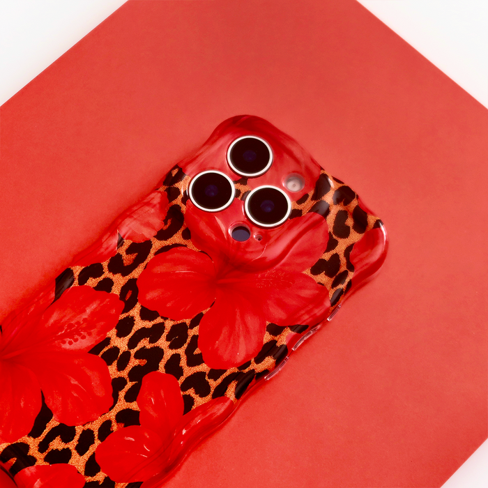Coconut Lane Wavy Phone Case in leopard and hibiscus print shown with a smartphone on a bright red surface.